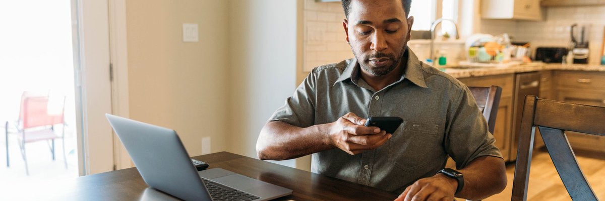 Man sits at counter with phone on laptop utilizing online banking.