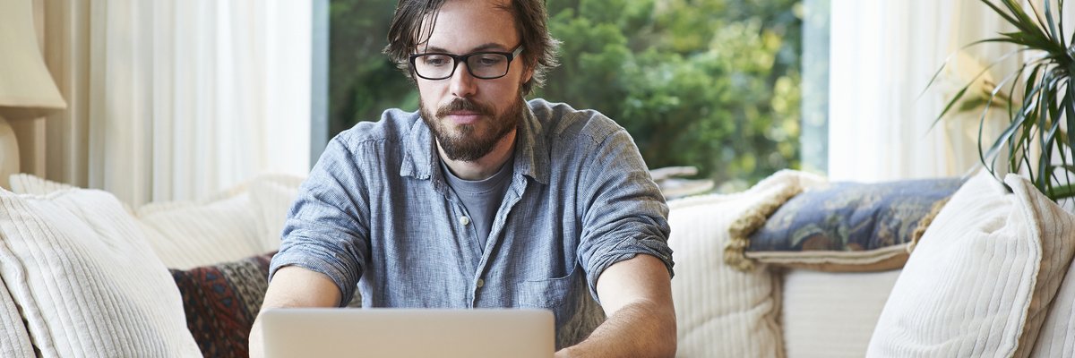 Man sitting on sofa and using laptop at home.