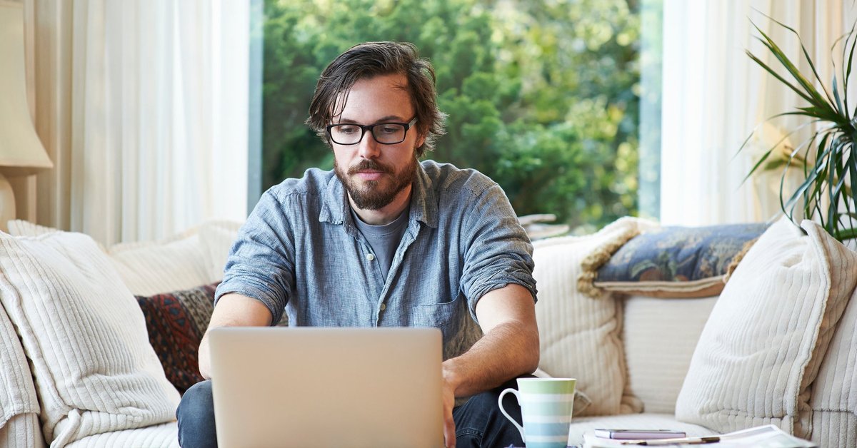 Man sitting on sofa and using laptop at home.