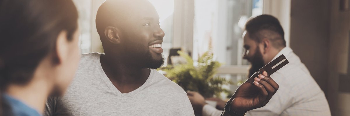 Man smiling at a restaurant and holding out a credit card.