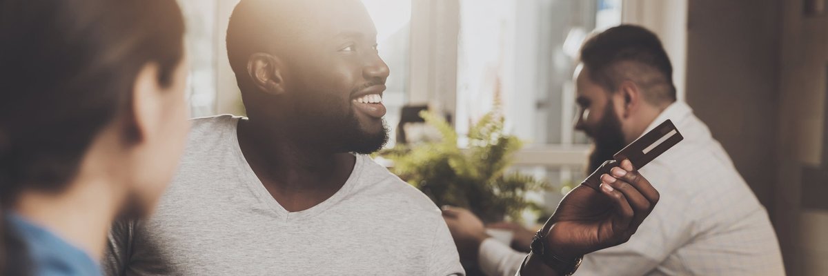 Man smiling at a restaurant and holding out a credit card.