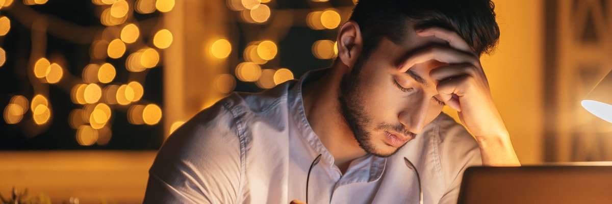 A man sitting in front of a laptop with his head resting in his hand.