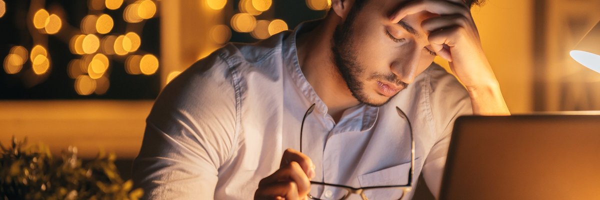 A man sitting in front of a laptop with his head resting in his hand.