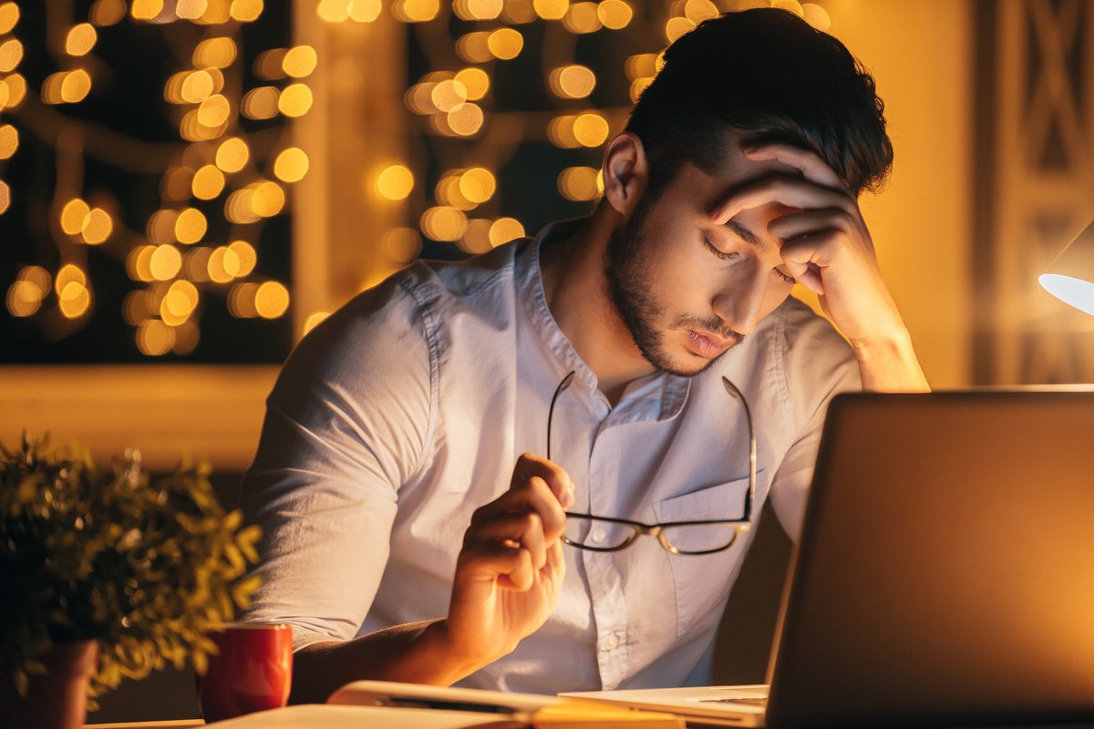 A man sitting in front of a laptop with his head resting in his hand.