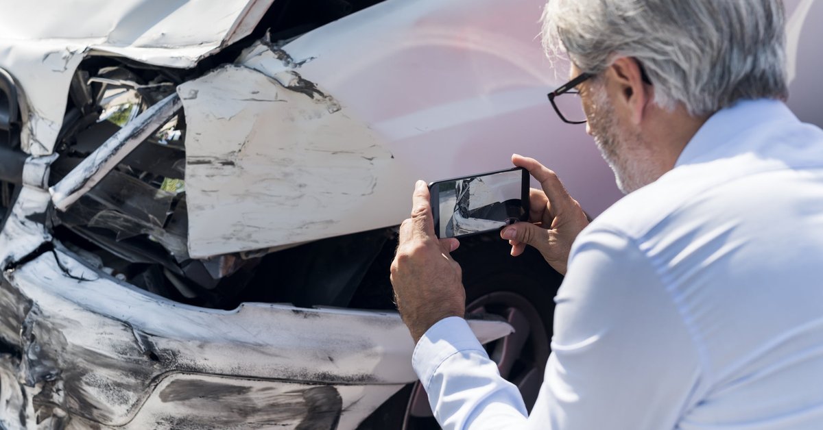 Man taking photos of damage to a vehicle.