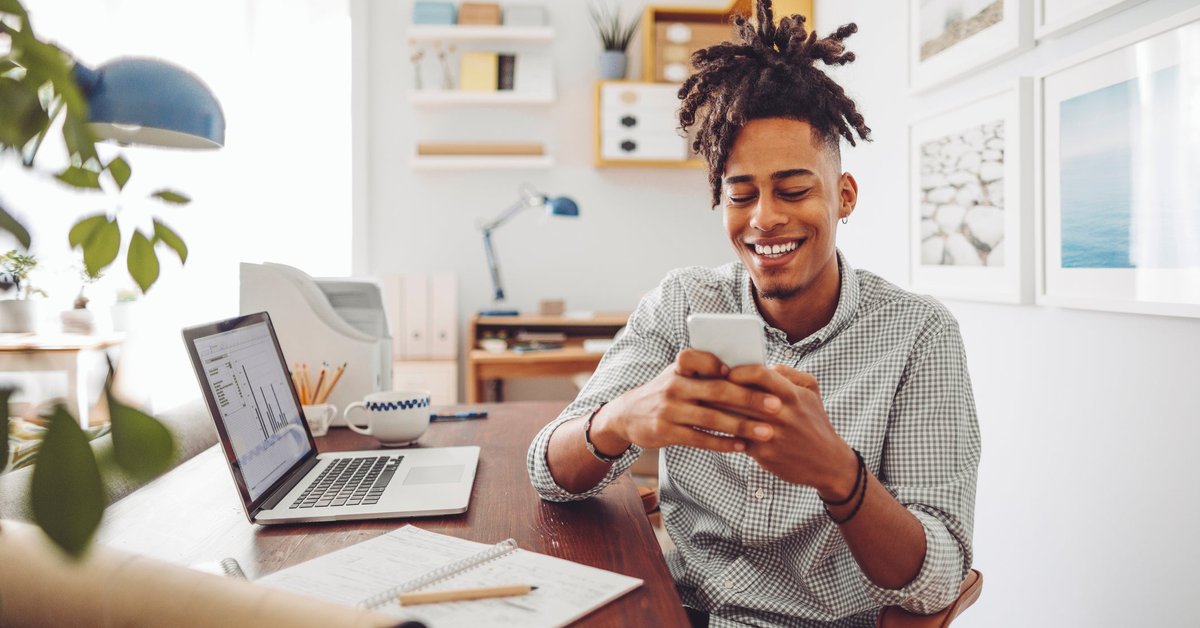 Man using his smartphone while laptop with data sits in the background.