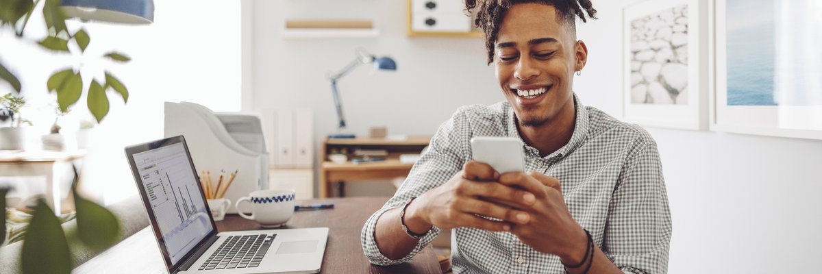 Man using his smartphone while laptop with data sits in the background.