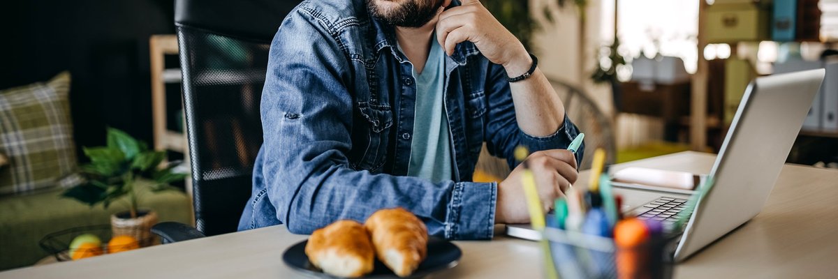 Man with glasses using laptop looks away appearing to be in thought.