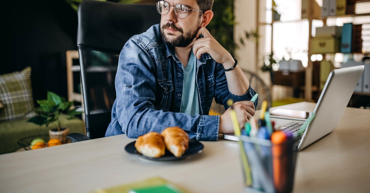 Man with glasses using laptop looks away appearing to be in thought.