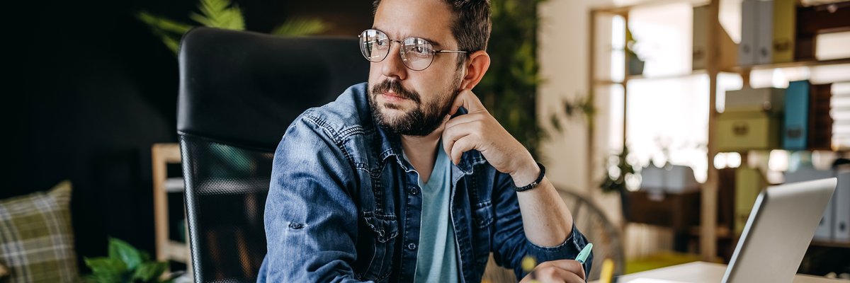 Man with glasses using laptop looks away appearing to be in thought.