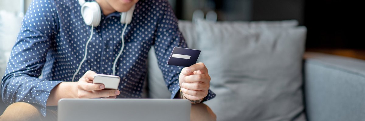 A young man holding a credit card and phone in front of a laptop.