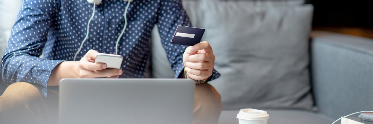 A young man holding a credit card and phone in front of a laptop.