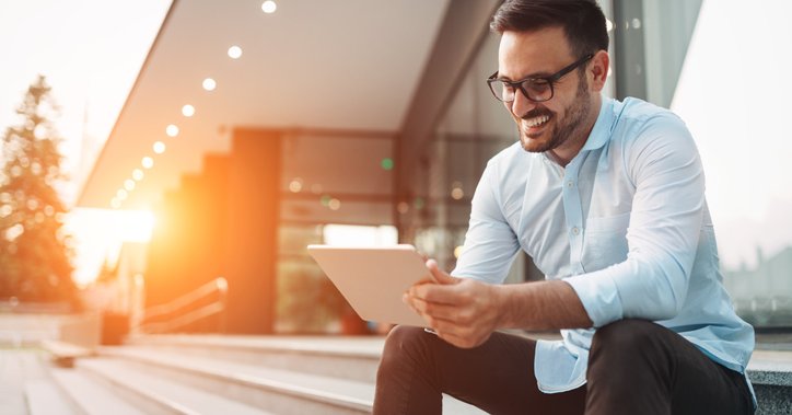 Smiling man using a tablet on the steps outside a building.