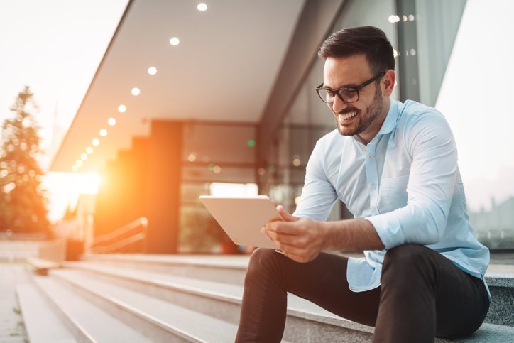 Smiling man using a tablet on the steps outside a building.