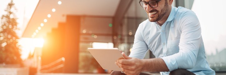 Smiling man using a tablet on the steps outside a building.