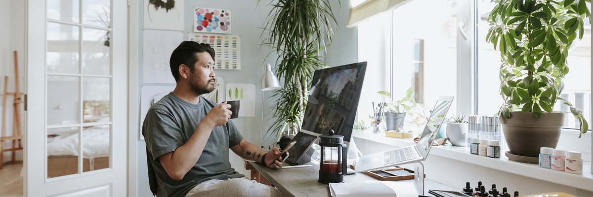 A man, working from home, sips his coffee and looks at his computer screen.