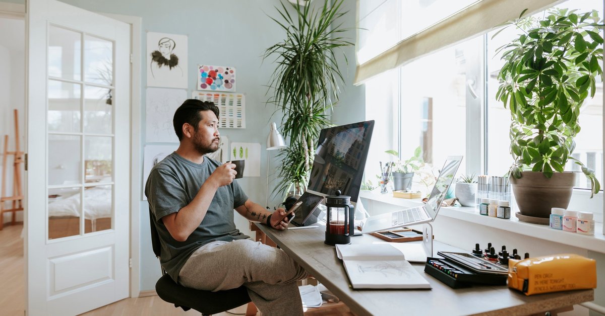 A man, working from home, sips his coffee and looks at his computer screen.