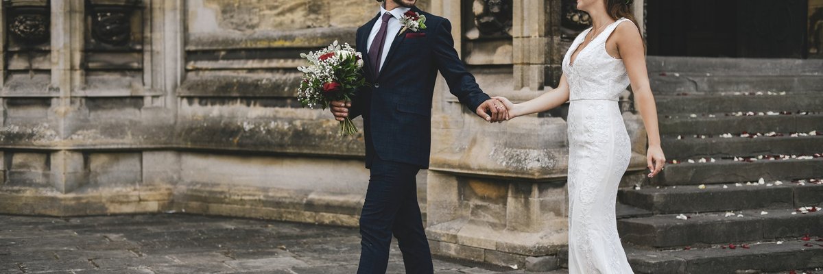 A married couple walking out of church holding hands and looking at each other.