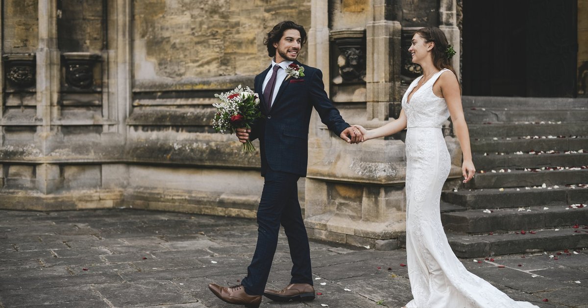 A married couple walking out of church holding hands and looking at each other.