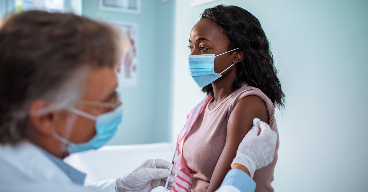 Masked woman receives injection in her arm from masked medical professional.