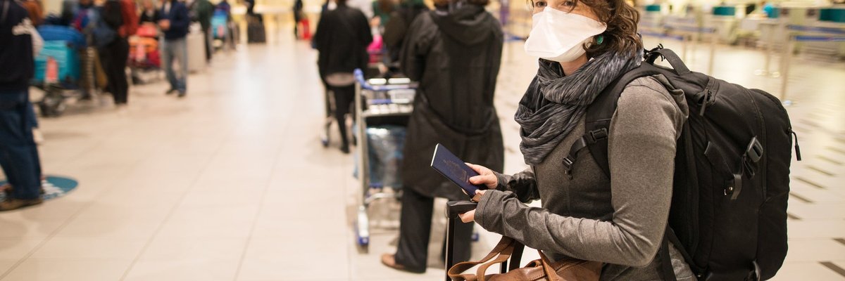 Masked woman with luggage waiting in a busy airport.