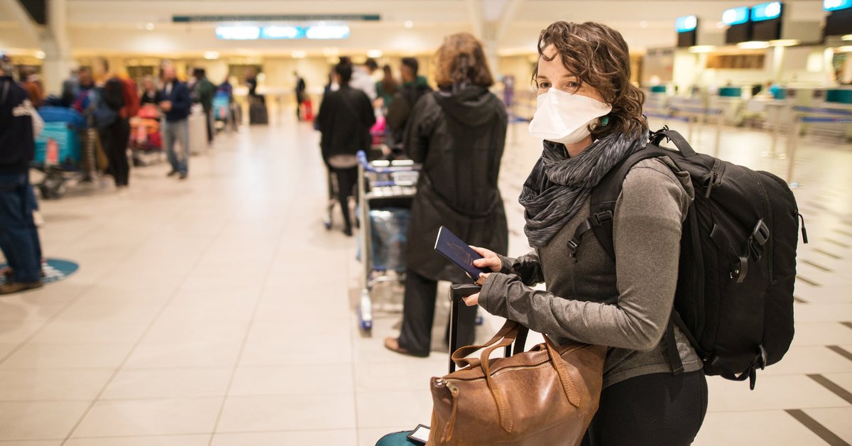 Masked woman with luggage waiting in a busy airport.