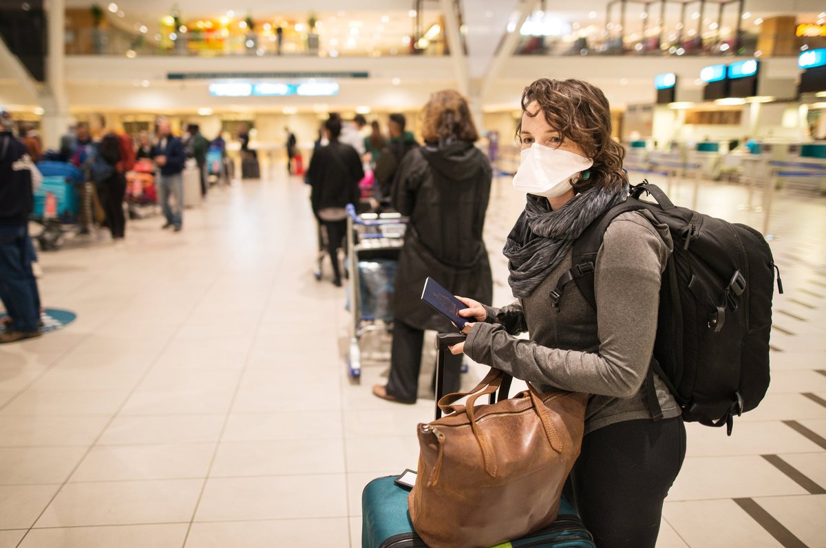 Masked woman with luggage waiting in a busy airport.