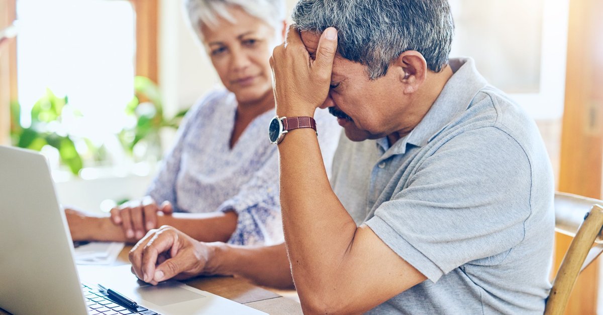 Mature couple appears distraught while looking at laptop.