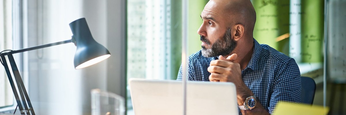 Mature man at desk looking off in thought.