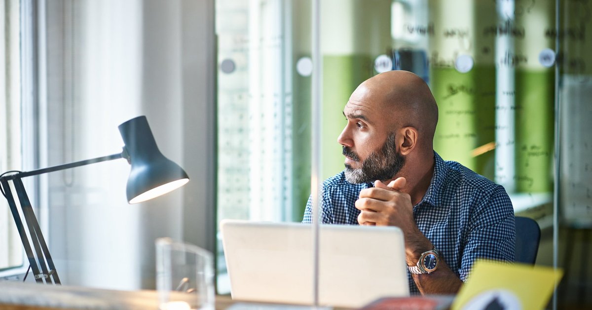 Mature man at desk looking off in thought.