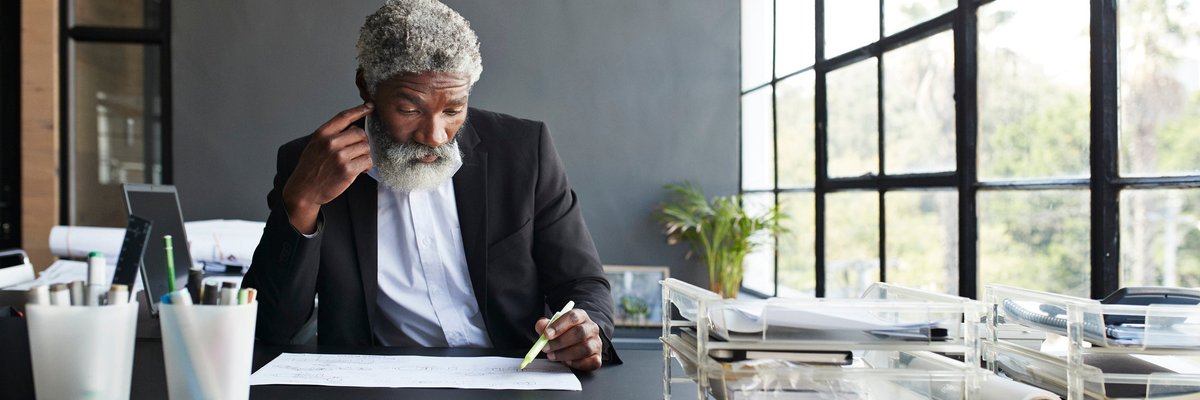 Mature man working on something at his desk in thought.