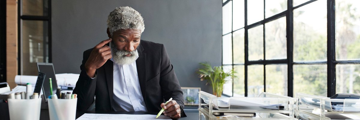 Mature man working on something at his desk in thought.
