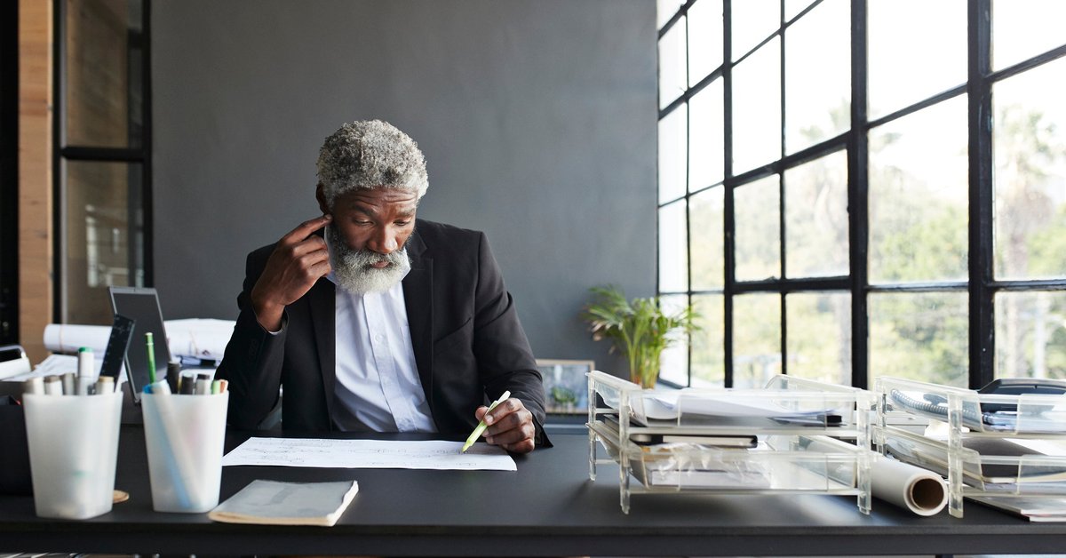 Mature man working on something at his desk in thought.