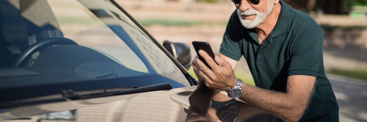 A mature man leans on his car as he looks at his phone.