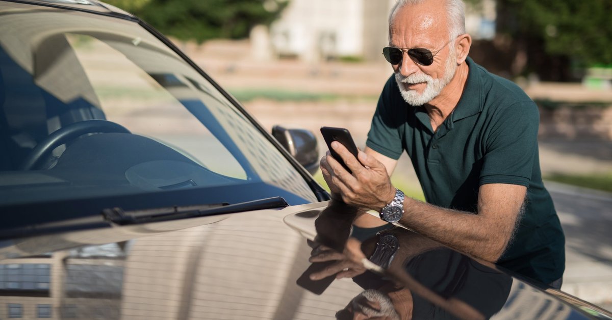 A mature man leans on his car as he looks at his phone.