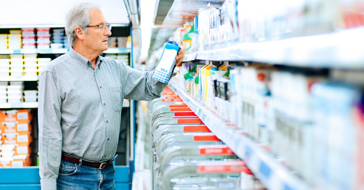 Mature man reads the label on a milk carton.