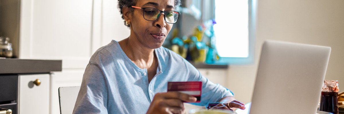 Mature woman hold credit card thoughtfully while using her laptop