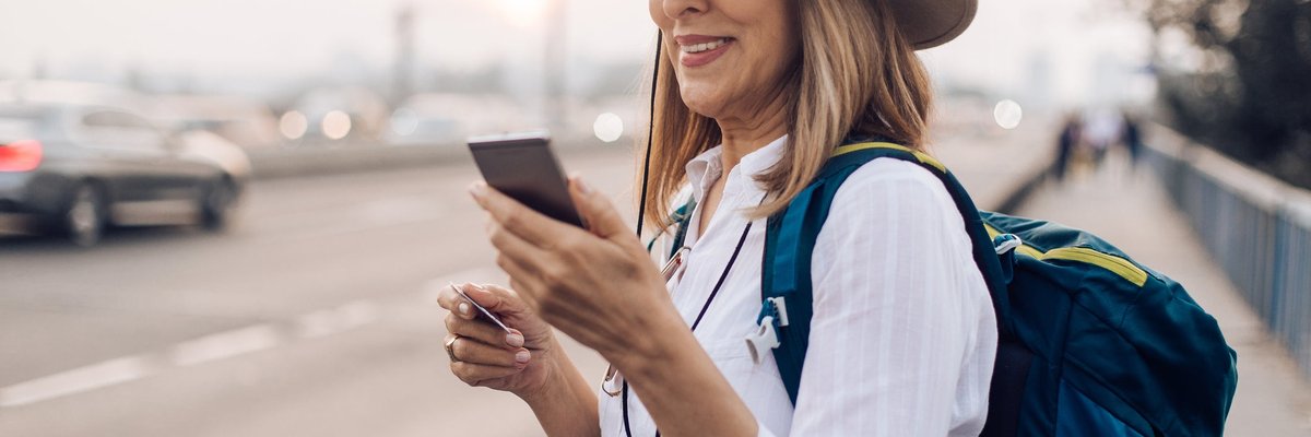 Mature woman holding her phone and a credit card while commuting with a backpack.