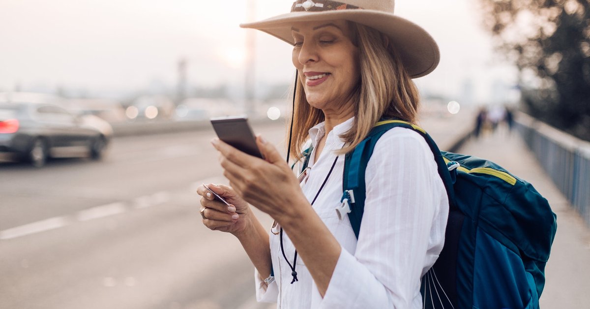 Mature woman holding her phone and a credit card while commuting with a backpack.