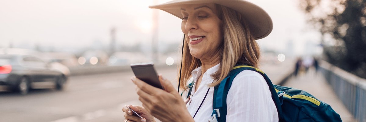 Mature woman holding her phone and a credit card while commuting with a backpack.