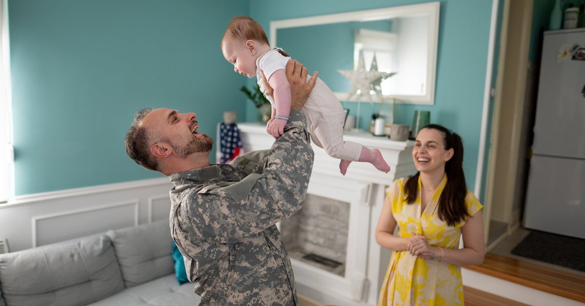 Military family enjoying time together inside home with toddler.