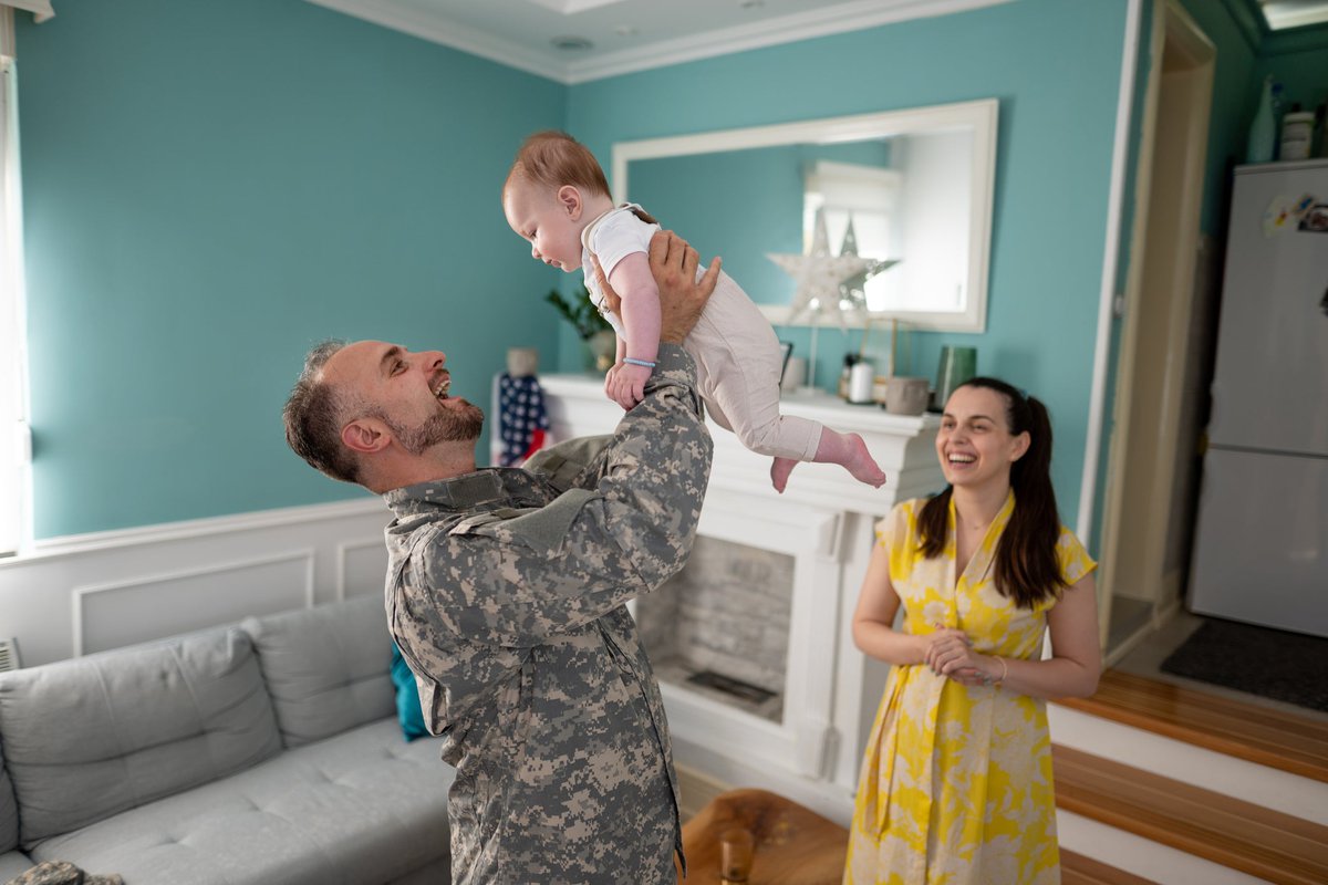 Military family enjoying time together inside home with toddler.