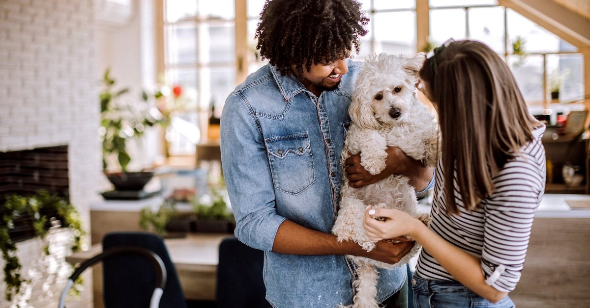 Millennial couple holding dog inside home.