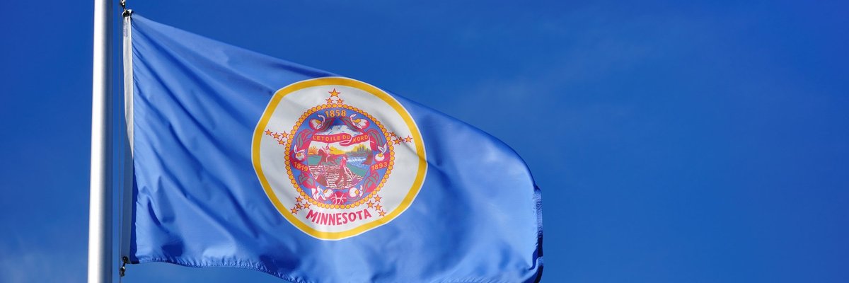 The Minnesota state flag waving in front of a blue sky.