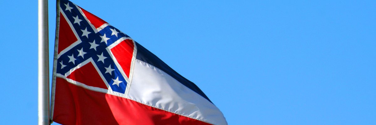 The Mississippi state flag flying in front of a blue sky.
