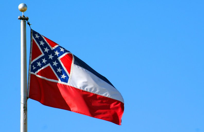The Mississippi state flag flying in front of a blue sky.