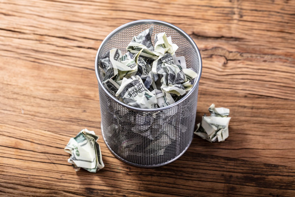 Crumpled dollar bills in a trash can.