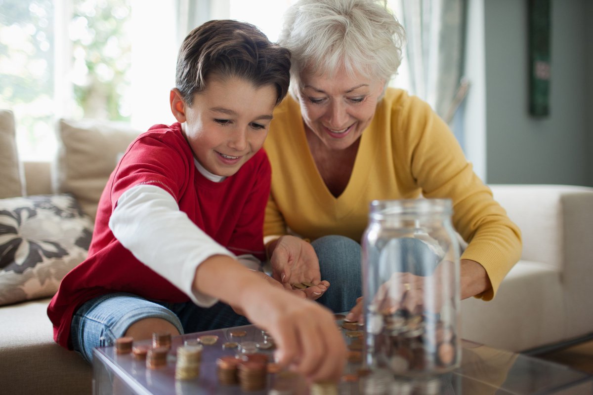 Grandmother teaching boy how to save coins in a jar.