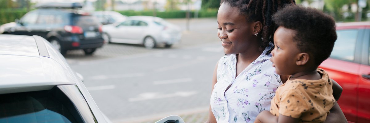 Mother holding her son while charging her electric vehicle
