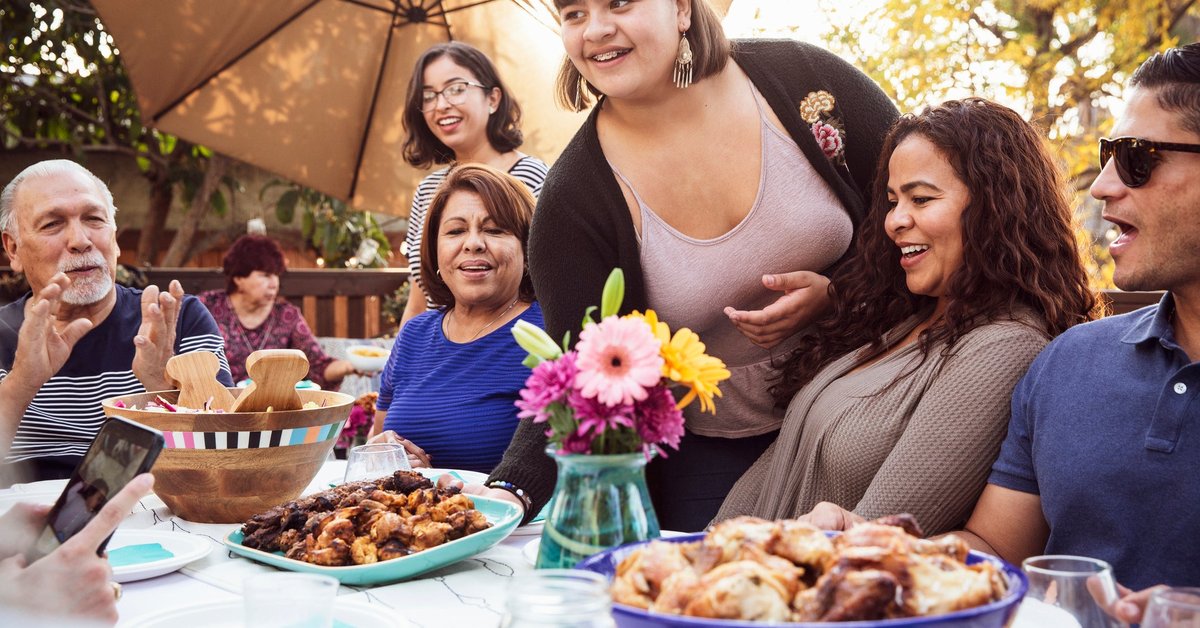 Multiple generations of people sharing a meal outdoors.